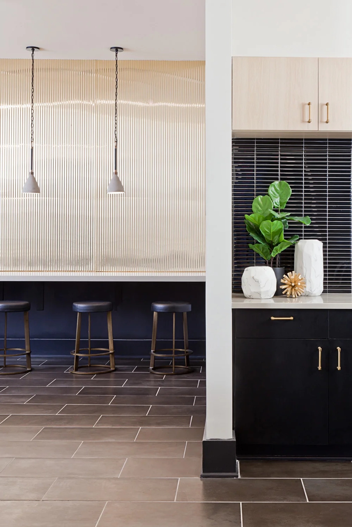 Clubhouse bar counter detail with navy leather stools, ribbed glass partition wall, black cabinetry with dark stacked tile backsplash, and decorative marble vase with fiddle leaf fig plant