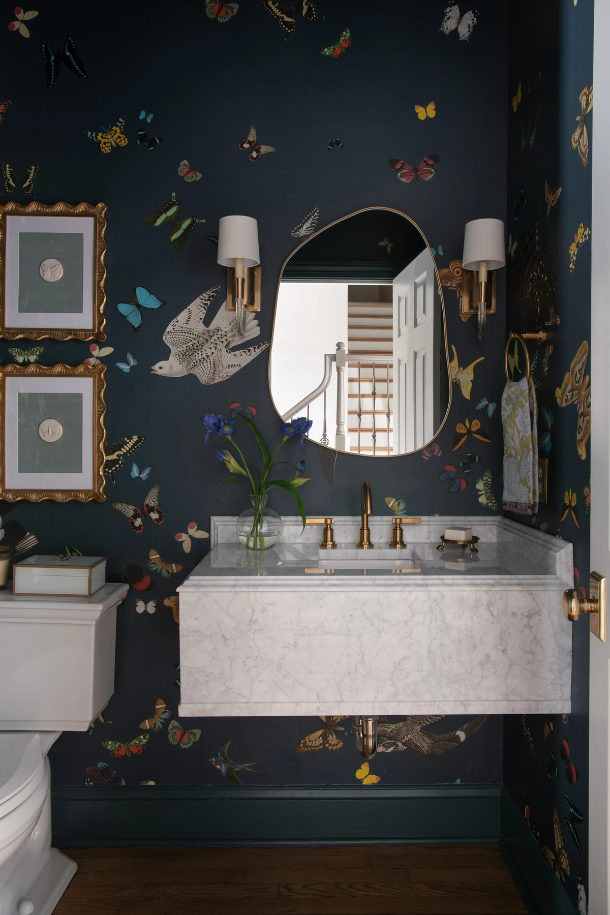 Powder bath with navy butterfly and bird wallpaper, marble vanity, and brass fixtures