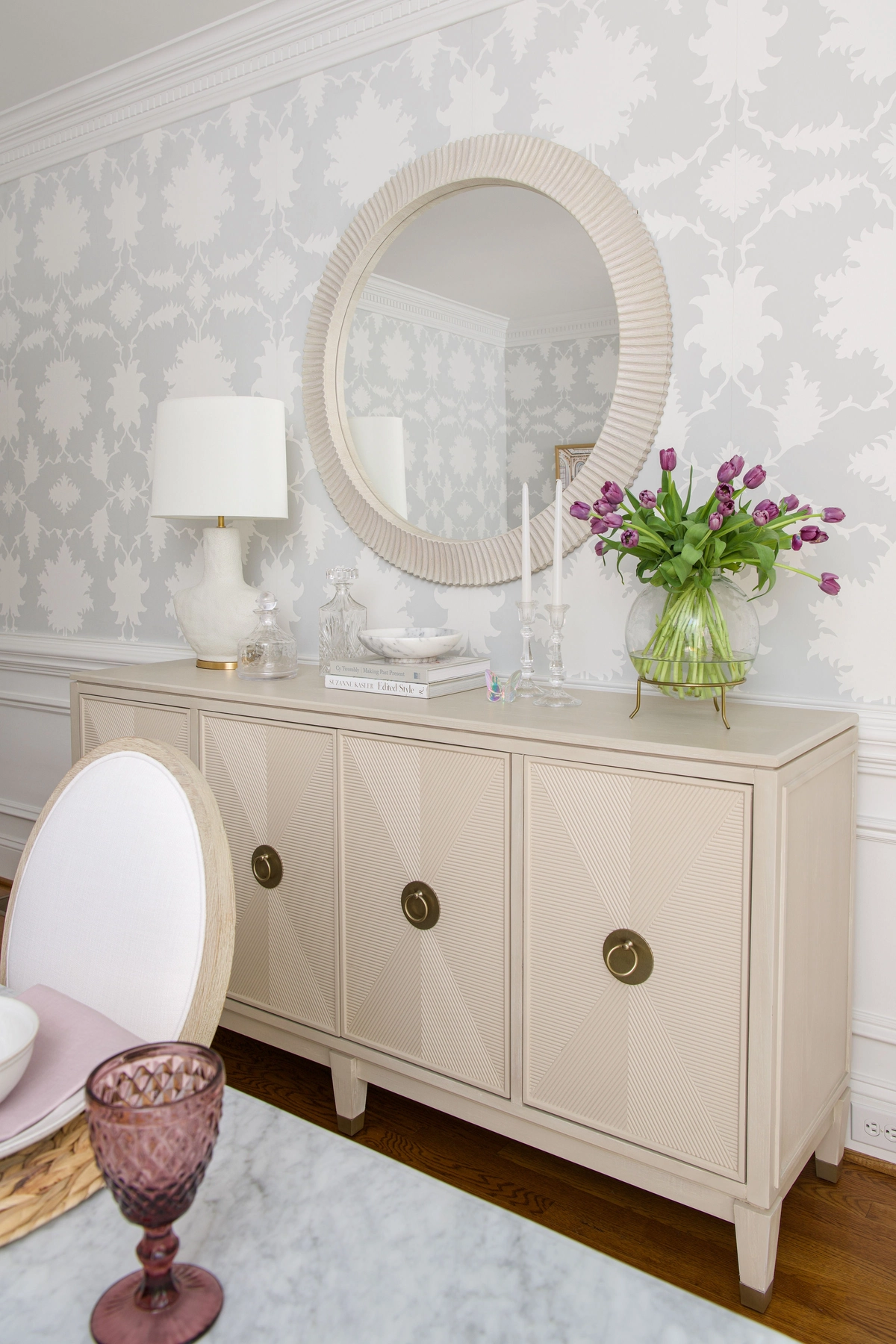 Dining room buffet with round mirror, fresh tulips, and damask wallpaper