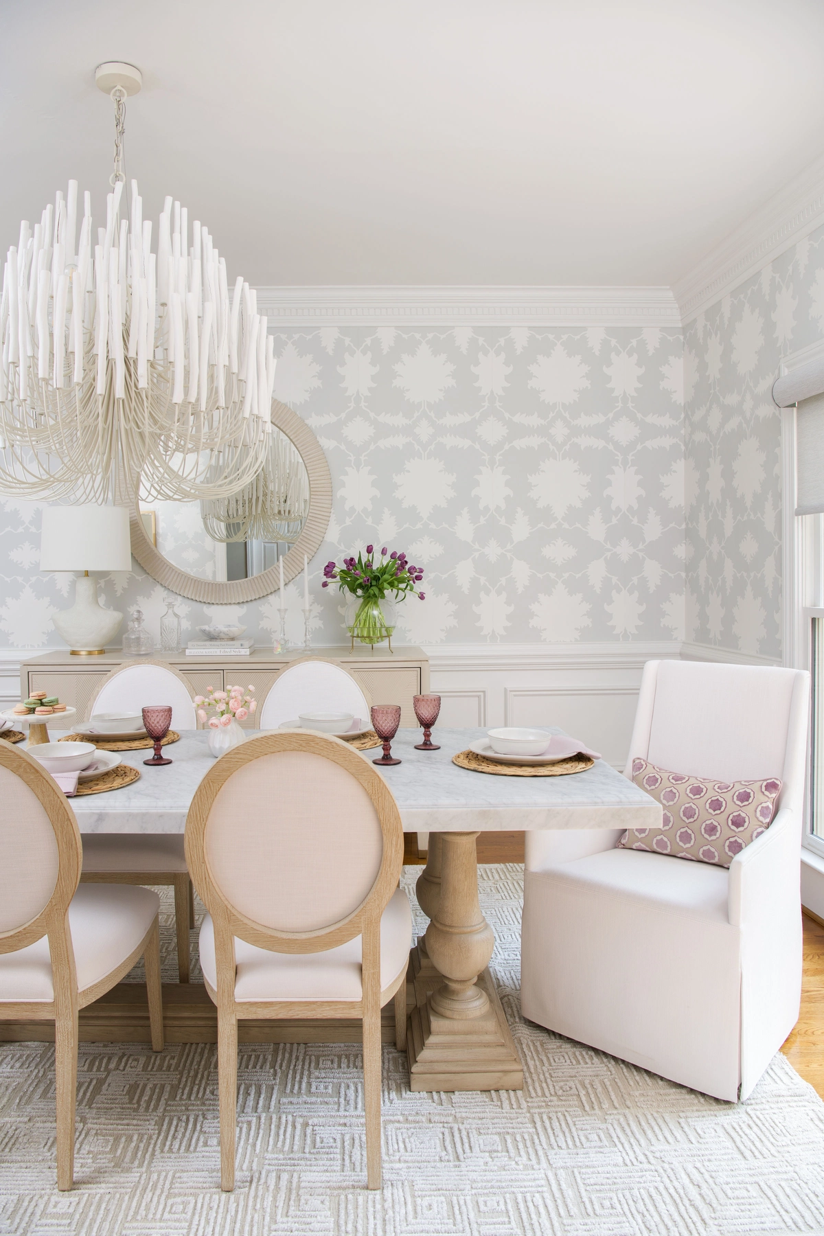 Corner view of the dining room with statement chandelier, upholstered host chairs, and patterned accent pillow