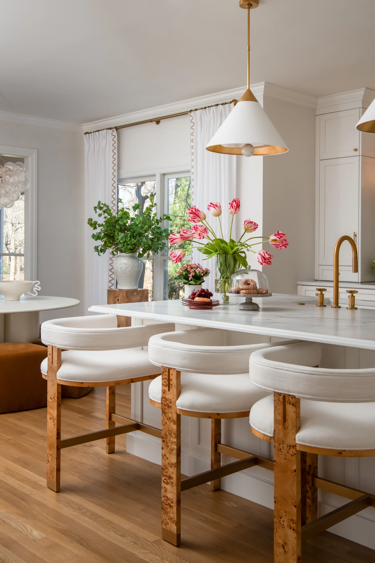 Kitchen island with burl wood bar stools, pendant lights, and fresh pink tulips