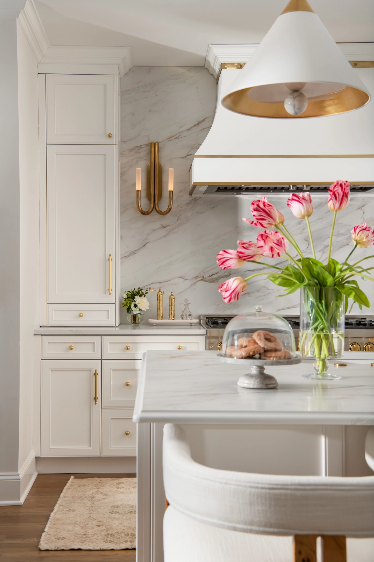 Marble backsplash detail with brass sconces, range hood, and parrot tulips on the island