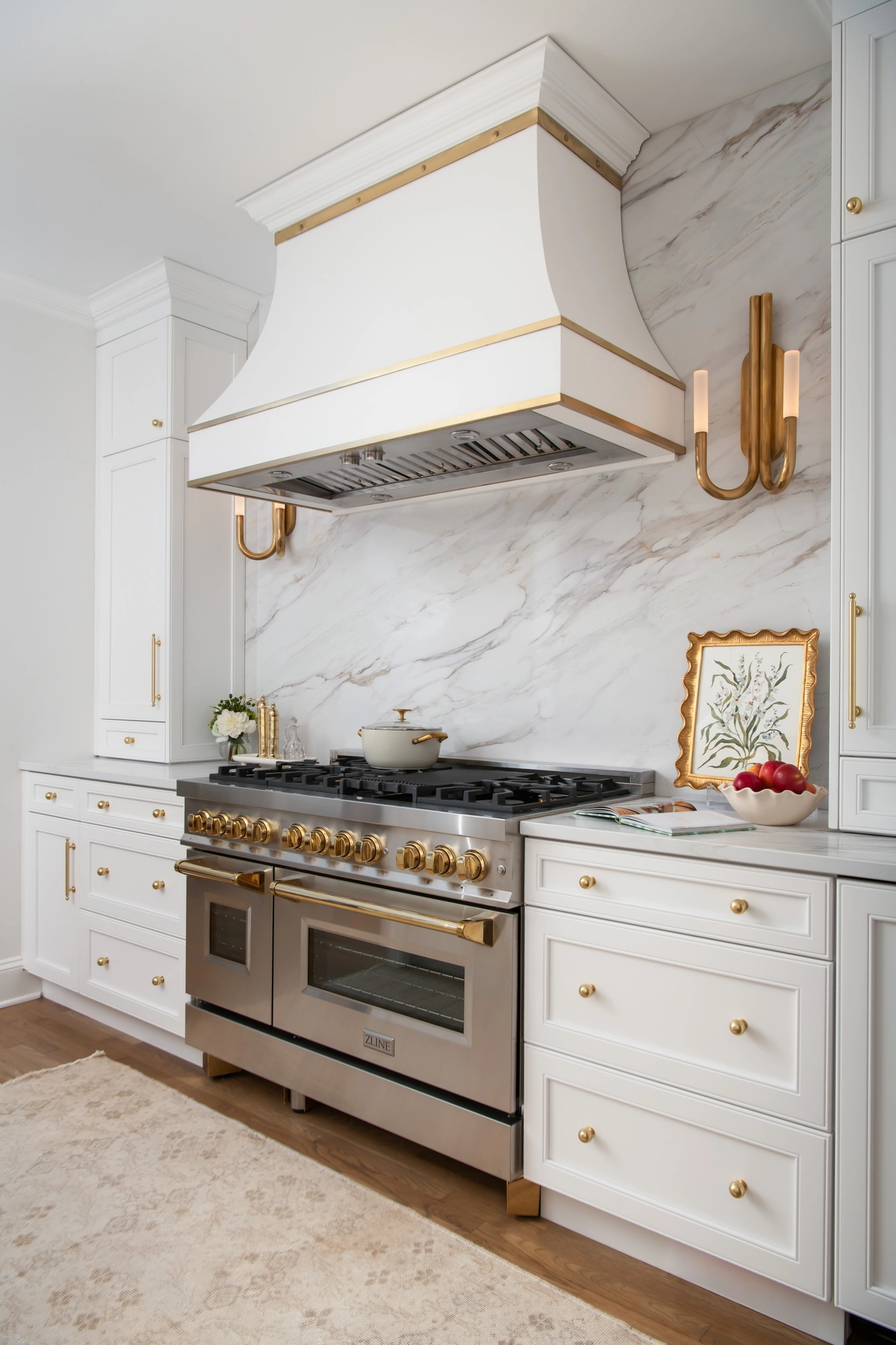 Custom range hood with brass trim, marble backsplash, professional range, and brass sconce lighting