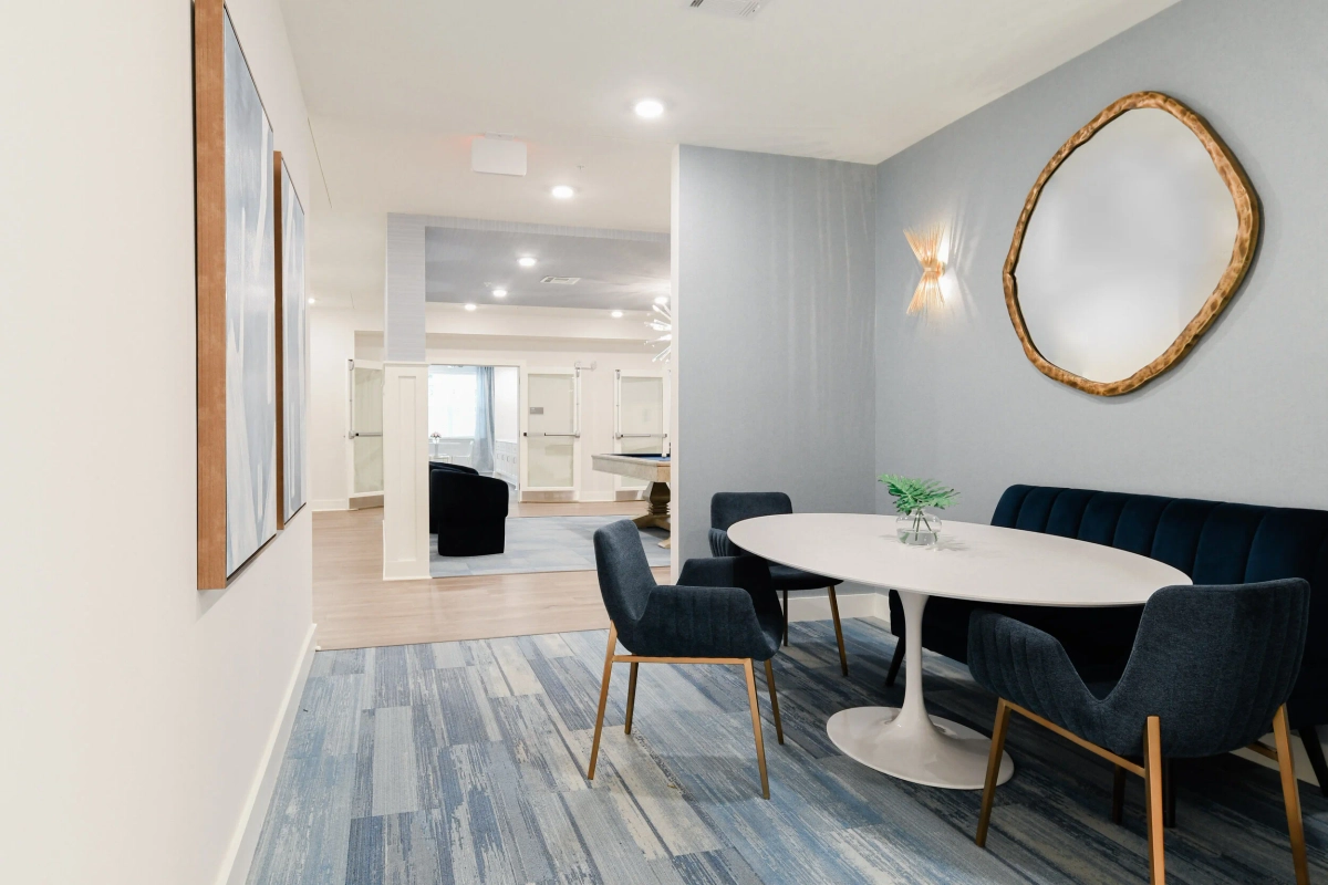 Intimate dining nook with navy blue channel-tufted banquette, navy velvet chairs, white tulip table, gold organic-shaped mirror, gold star wall sconce, and blue-toned plank flooring