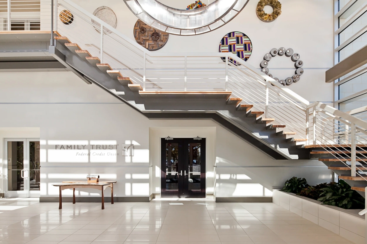 Grand office entrance hall with Family Trust signage above glass double doors, open-tread staircase with wood treads and cable railing, circular decorative art pieces on the upper wall