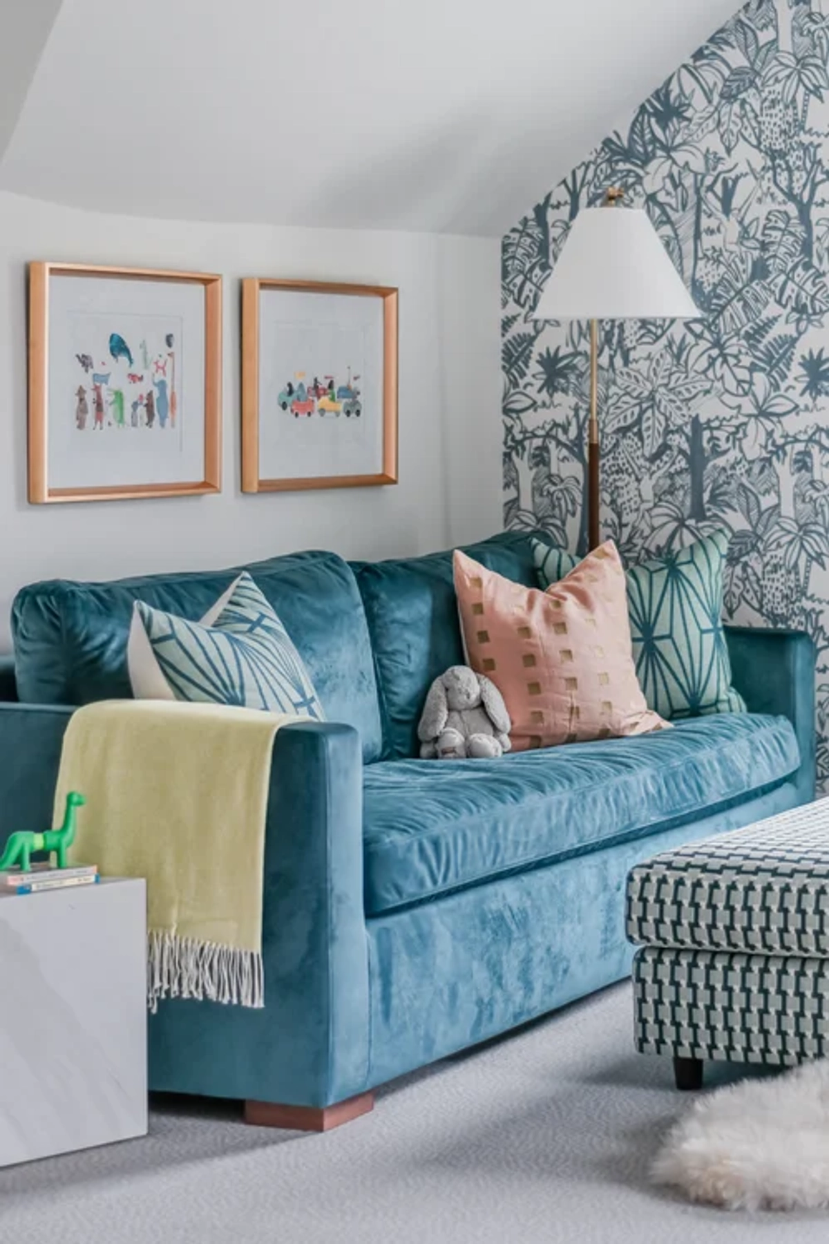 Teal velvet sofa with pink and turquoise throw pillows, set against a blue-and-white jungle toile wallpaper, flanked by two framed prints
