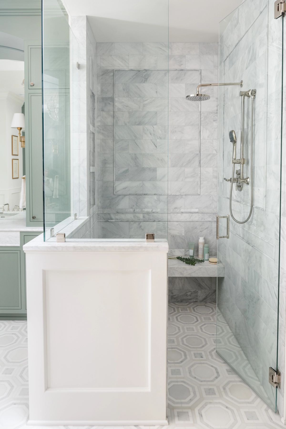 Primary bathroom walk-in shower with marble tile walls in a herringbone pattern, frameless glass enclosure, polished nickel fixtures, and a built-in corner bench