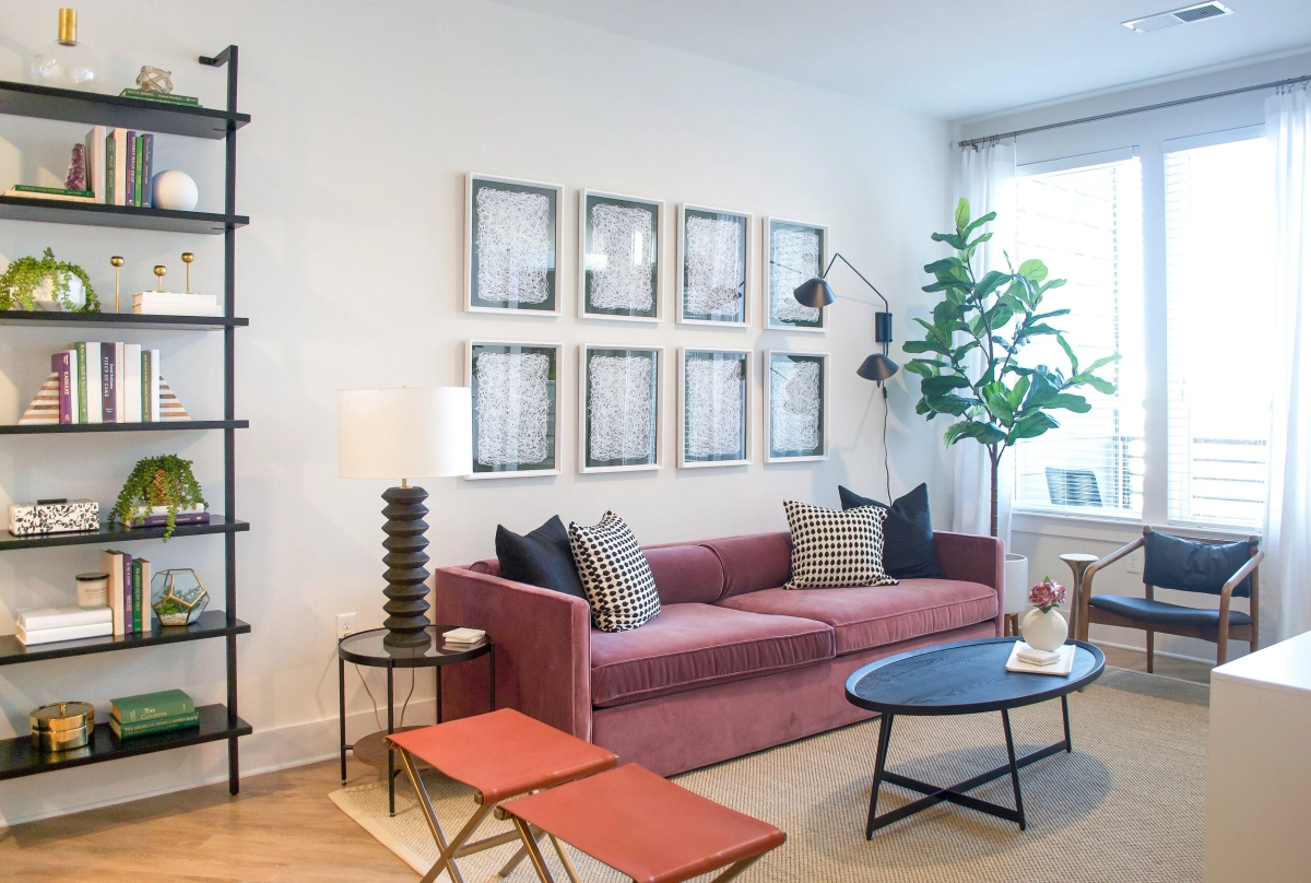Wide living room view featuring a mauve velvet sofa with patterned pillows, a black metal open bookshelf with styled decor, a gallery wall of six abstract prints, and a fiddle leaf fig