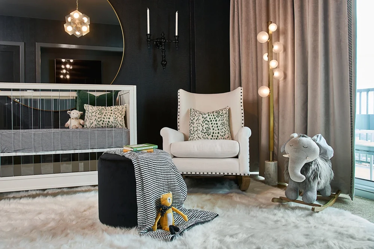Dramatic nursery with black walls, a mirrored crib, a cream wingback rocking chair with leopard-print pillows, a plush elephant rocker, and modern globe lighting